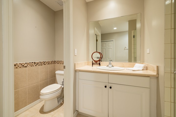 Modern bathroom with a sink, mirror, and toilet. Beige tiles and a white cabinet are visible.