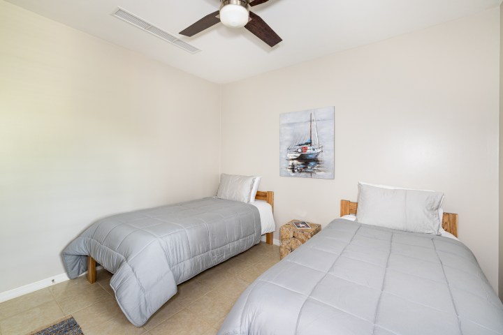 Simple bedroom with two twin beds, grey comforters, and a painting of a boat on the wall.