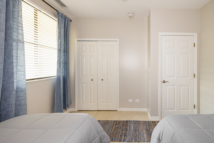Bedroom with two beds, blue curtains, and a closet and door on a beige wall.