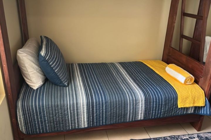 A neatly made bed with blue striped bedding, yellow blanket, and rolled towel.
