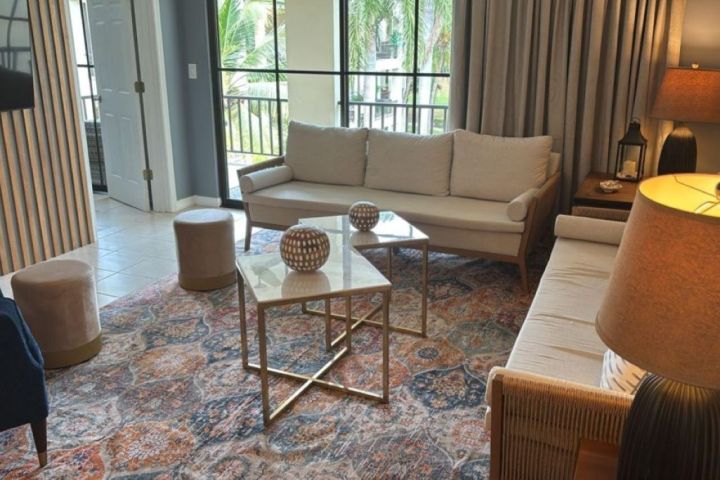 Modern living room with sofas, a patterned rug, and metallic coffee tables near a large window.