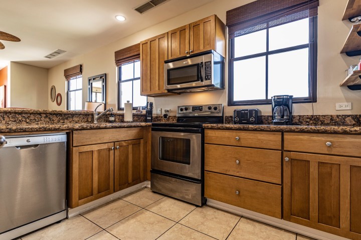 Modern kitchen with wooden cabinets, granite countertops, stainless steel appliances, and tile floor.