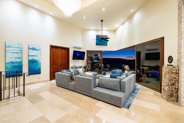 Spacious living room with a gray sofa, blue chairs, and large windows overlooking a sunset view.