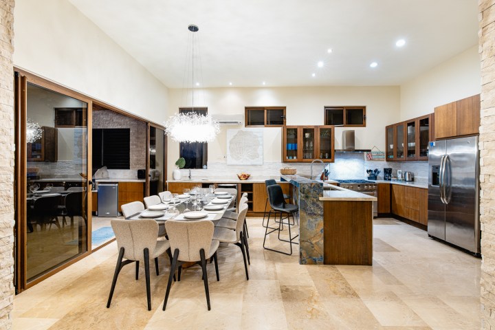 Modern kitchen and dining area with wood cabinets, island, and chandelier over a set dining table.