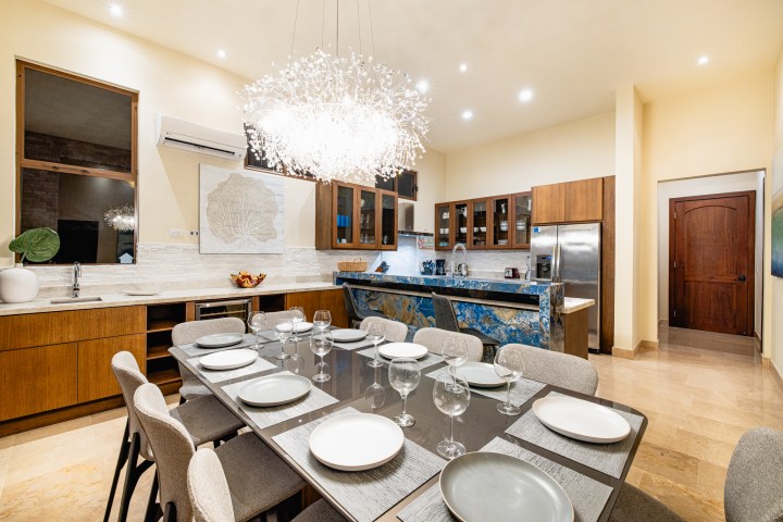 Modern dining room with a set table, open kitchen, and a large chandelier.