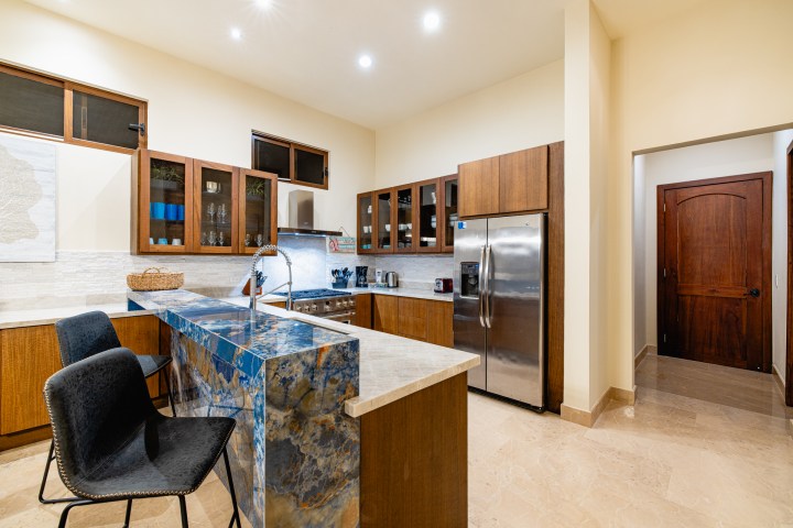 Modern kitchen with wood cabinets, marble countertops, and stainless steel fridge and appliances.