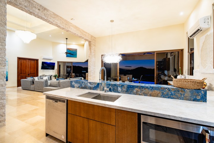 Modern kitchen with blue marble countertop, living area, and evening view through large sliding doors.