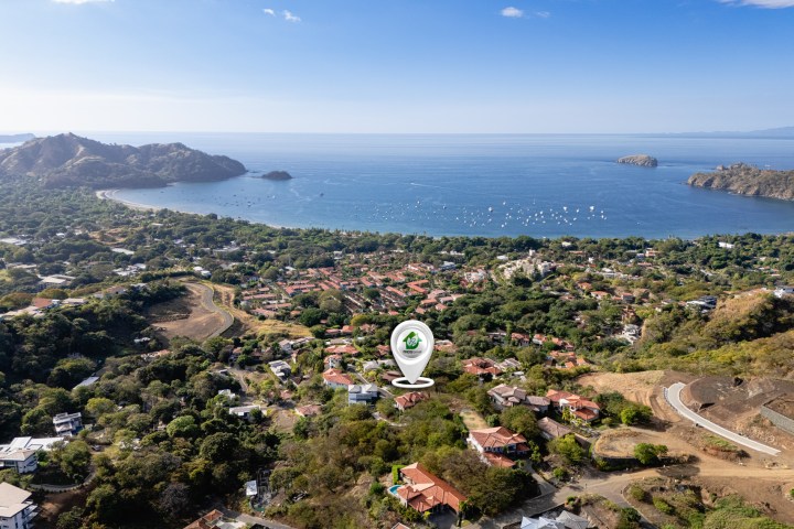 Aerial view of a coastal town with lush greenery, red roofs, and a bay with boats.
