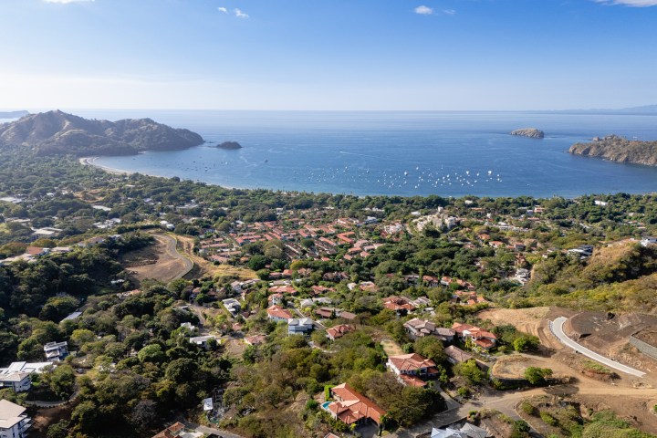 Aerial view of a coastal town with lush greenery and a bay with boats.