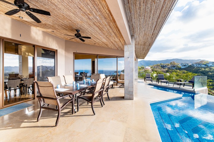Covered patio with dining set, ceiling fans, and adjacent infinity pool overlooking a scenic mountain view.