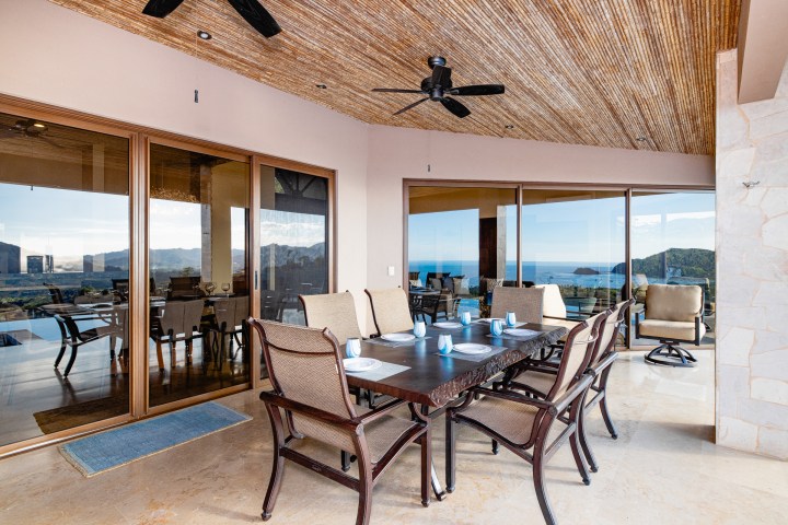 Outdoor dining area with ocean view, table set for eight, under a ceiling fan.