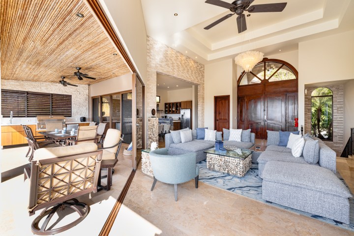 Spacious living room with large sectional sofa, glass table, open kitchen, and sliding doors to patio area.