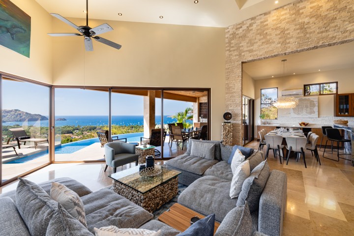 Spacious living area with ocean view, modern furniture, and large sliding glass doors to a poolside patio.