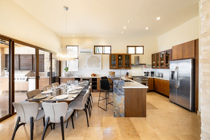 Modern kitchen and dining area with wooden cabinets, island, and large dining table set for eight.