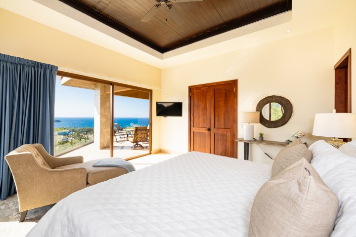 Bright bedroom with ocean view, large bed, armchair, sliding glass doors, and balcony.