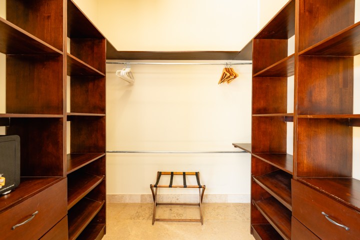 Empty walk-in closet with wooden shelves, hangers, and a luggage rack.