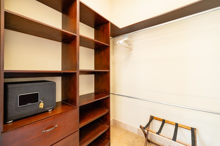 Closet with wood shelves, safe, hanging rod, hangers, and luggage rack.