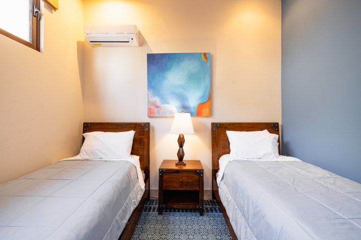 Twin beds with a lamp and an abstract painting on the wall, in a softly lit room.