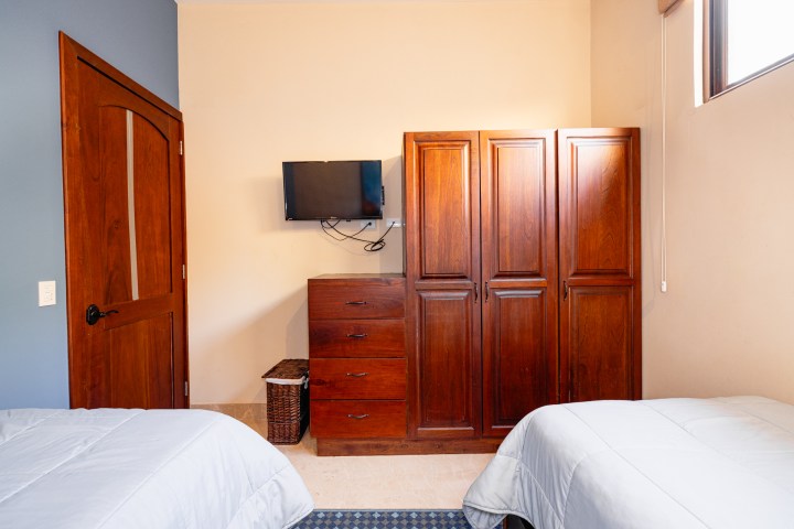 Bedroom with two beds, wooden wardrobe, dresser, and wall-mounted TV.