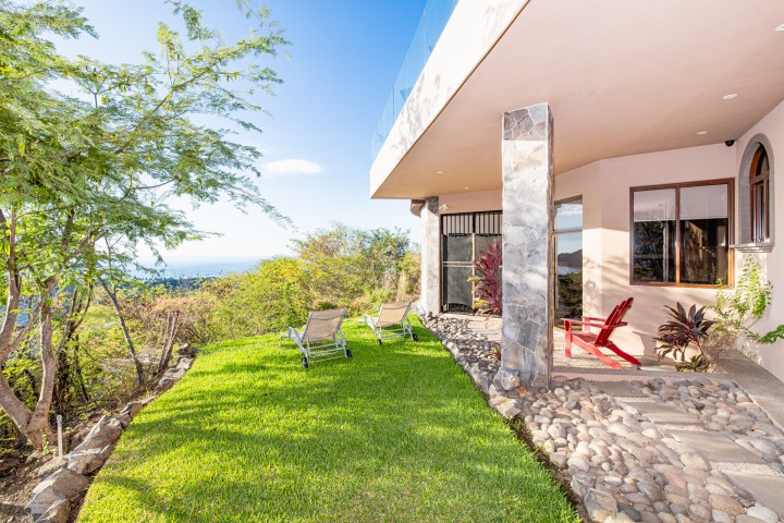 Modern terrace with two loungers on grass, trees, and ocean view.