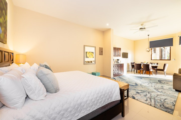 Spacious bedroom with white bed, blue rug, dining area, and wall art.
