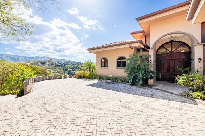 Mediterranean-style house with arch doorway and large driveway under a clear sky.