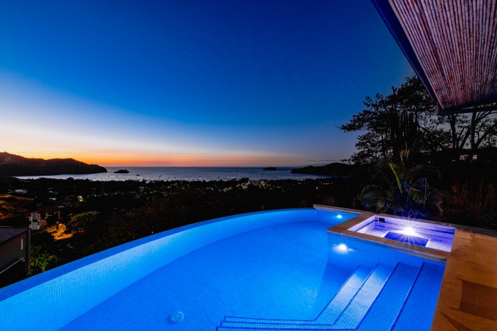 Infinity pool overlooking ocean at sunset with illuminated water and coastal view.
