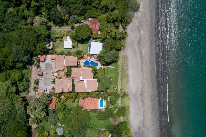 Aerial view of beachfront property with buildings, pools, and lush greenery.