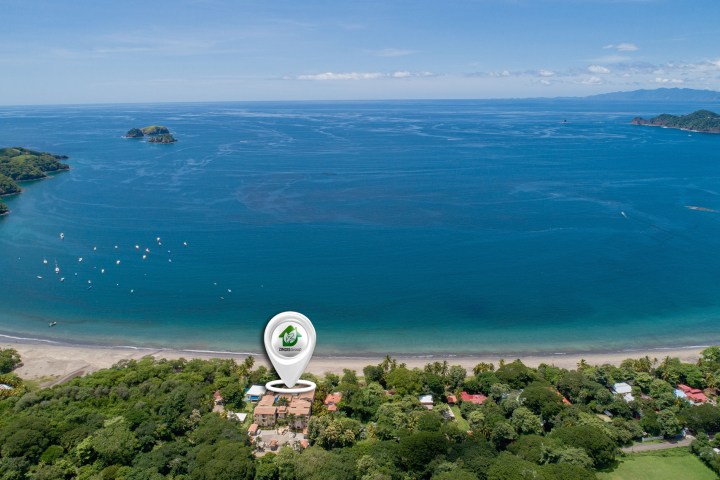 Aerial view of a coastline with beach, ocean, islands, and a location pin marked Indexhouse.