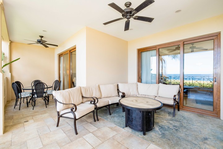 Outdoor patio with wicker furniture, round table, ceiling fans, and sliding glass doors overlooking a view.