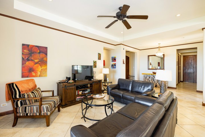 Cozy living room with dark furniture, colorful art, ceiling fan, and tiled floor.