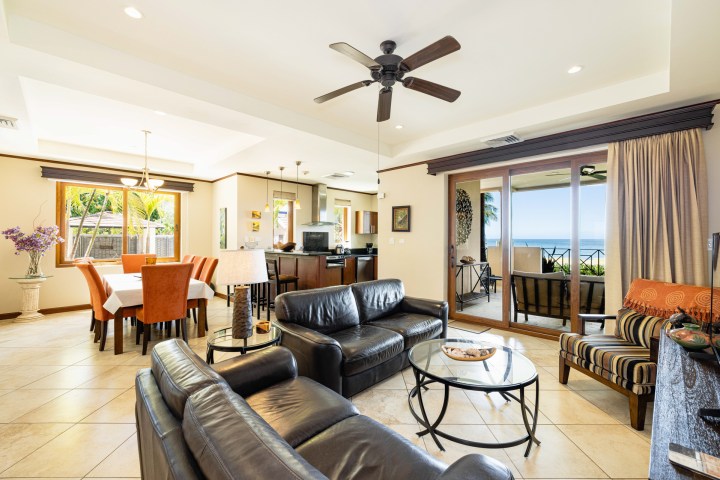 Spacious living room with leather sofas, dining area, and ocean view through sliding glass doors.
