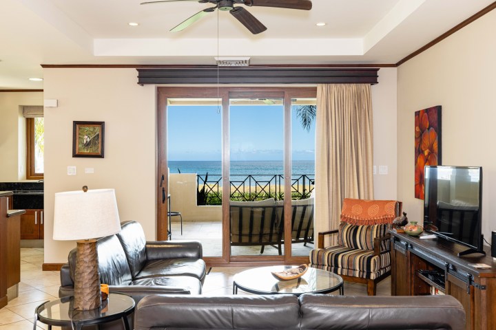 Modern living room with ocean view through glass doors, leather sofa, striped chair, and ceiling fan.