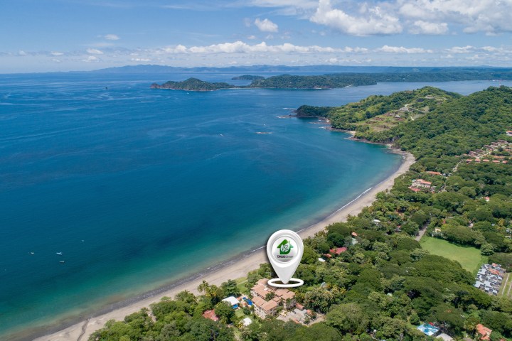 Aerial view of a coastal area with blue ocean, green hills, and buildings near the shore.