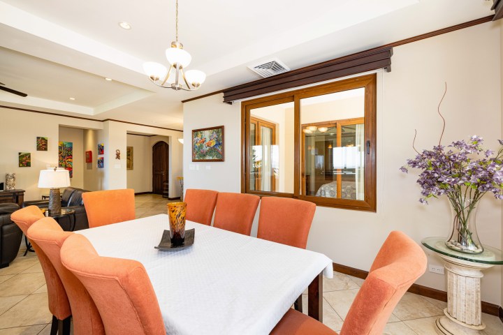 Dining room with orange chairs, white tablecloth, chandelier, and colorful artwork on walls.
