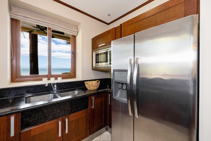 Modern kitchen with wooden cabinets, stainless steel fridge, and ocean view through a window.
