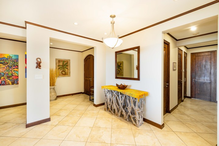 Interior with wooden doors, abstract art, branch table, mirror, and ceiling light on tiled floor.