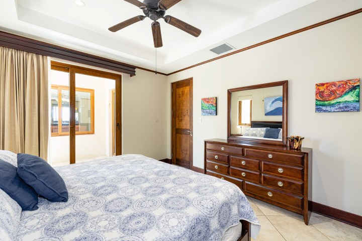 Bedroom with bed, dresser, mirror, ceiling fan, and sliding glass doors.