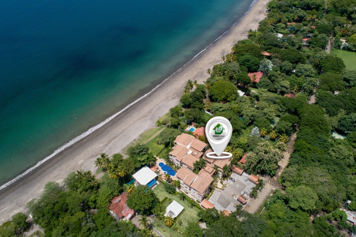Aerial view of beachfront property with lush greenery and a marked location pin.