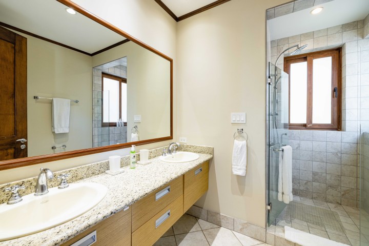 Modern bathroom with double sink, granite countertop, large mirror, and glass shower enclosure.