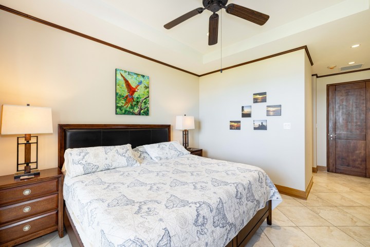 Bedroom with a ceiling fan, bed, two lamps, and artwork on walls.