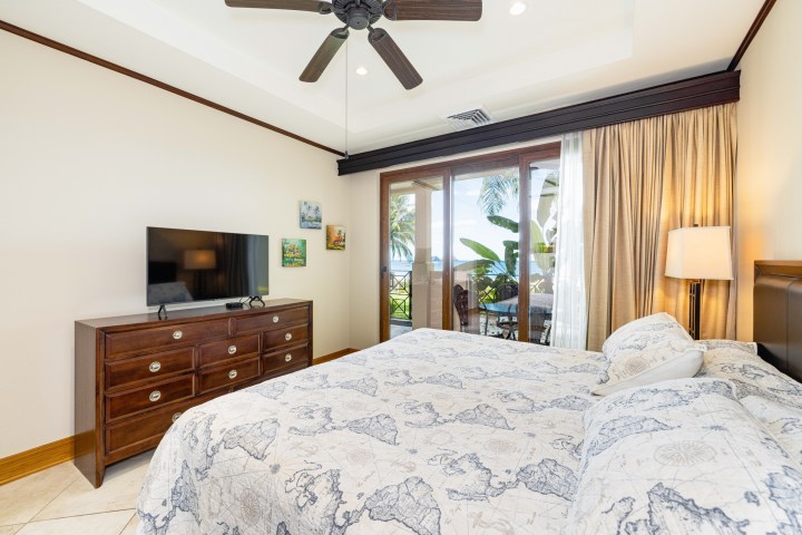 Bedroom with bed, TV on dresser, ceiling fan, and sliding doors to balcony with ocean view.