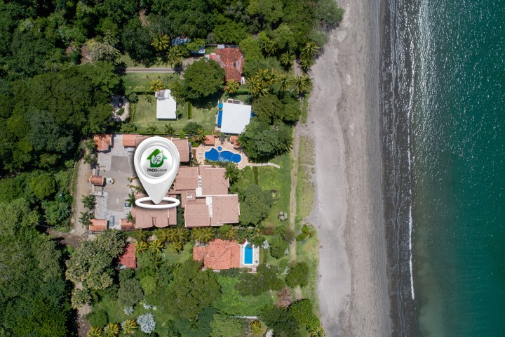 Aerial view of beachside property with trees, buildings, and pool.