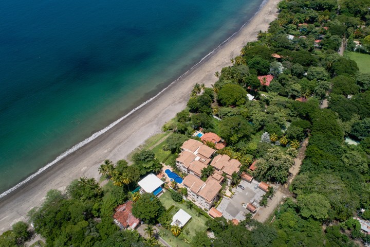 Aerial view of a beachfront resort with lush greenery and buildings near the ocean shore.