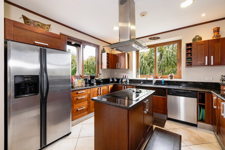Modern kitchen with wooden cabinets, island, stainless steel appliances, and large windows with green view.