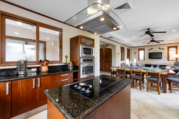 Modern kitchen with wooden cabinets, black countertops, and an open living room with dining area.