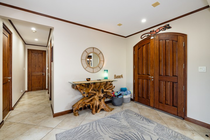Hallway with wooden doors, driftwood table, round mirror, and baskets on tiled floor.