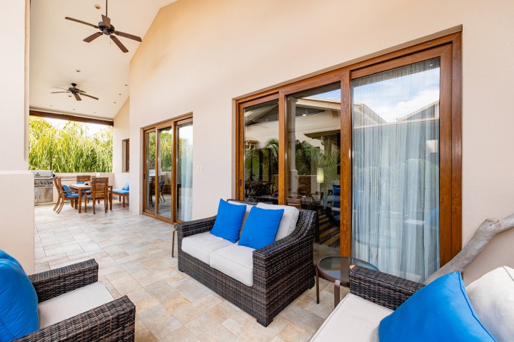 Outdoor patio with wicker furniture, blue cushions, ceiling fans, and a dining table under a covered area.