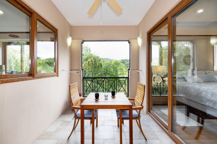 Balcony with table, two chairs, and view of trees, adjacent to sliding glass doors.