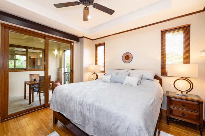 Modern bedroom with double bed, ceiling fan, balcony view, and two nightstands with lamps.